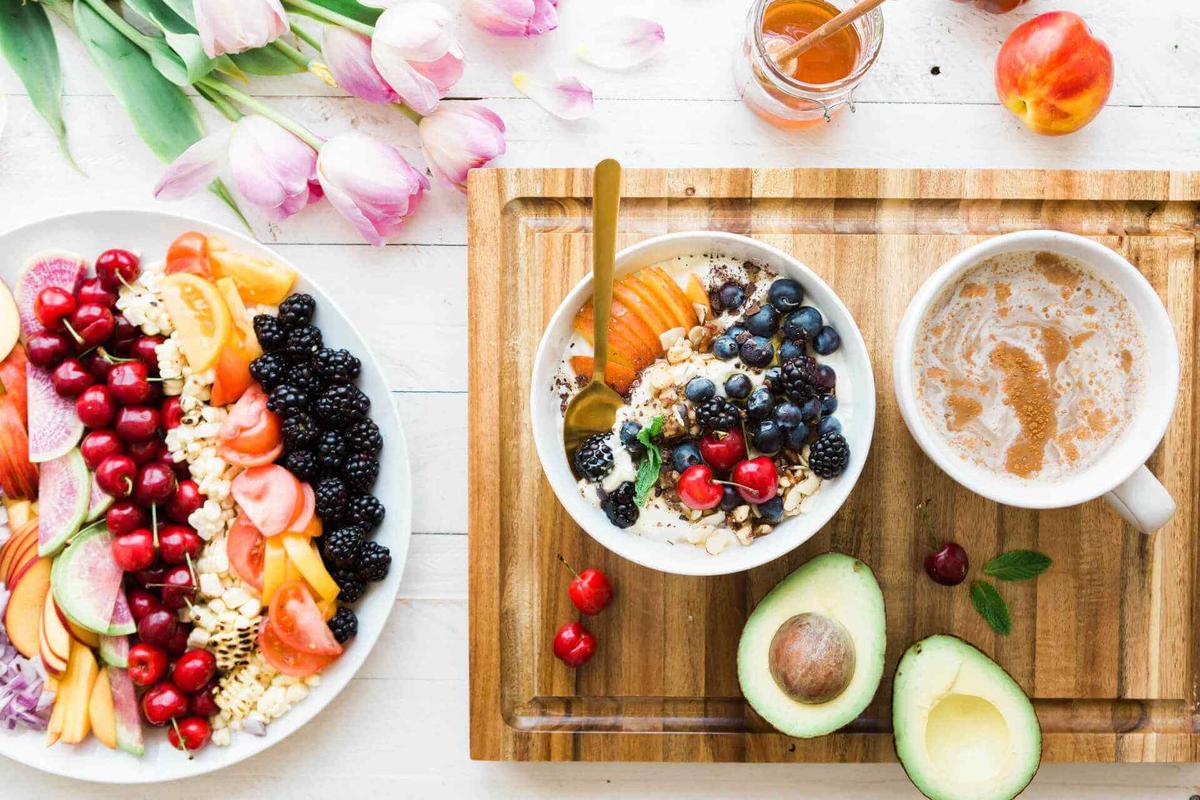 Appealing fruit and porridge bowl and halved avocado on wooden chopping board next to plate of sliced brainfood snacks